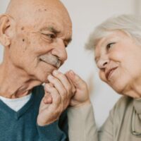 An elderly couple looking at each other with love while holding hands.