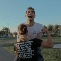Two people embracing, with one wearing a "No homophobia, no violence, no racism, no sexism, yes kidness, yes peace, yes equality, yes love" shirt.