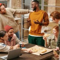 A diverse group of people hanging around a table.